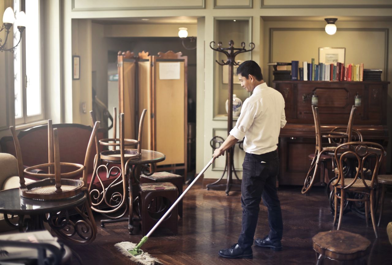 Side view of a young ethnic male in uniform cleaning the floor with a mop while working in a retro-style restaurant